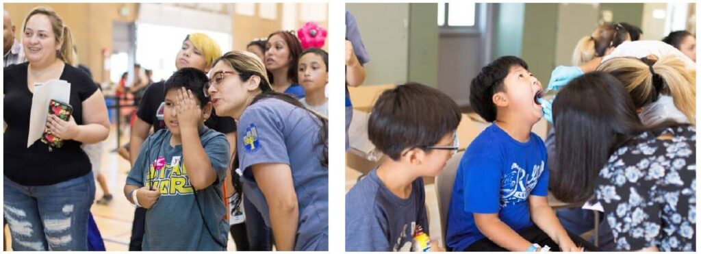 Two side-by-side photos from a community health event. Left photo: A healthcare worker wearing a blue shirt with a cross logo performs a vision screening on a young boy in a Star Wars t-shirt, covering one of his eyes, while a group of parents and children wait in line behind them inside a gymnasium. Right photo: A young boy in a blue t-shirt sits with his mouth wide open as a gloved healthcare professional performs an oral health screening, while another child sits nearby.