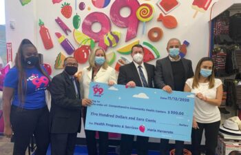 Six people stand indoors holding a large check for $500, with colorful decorations and products on shelves in the background.