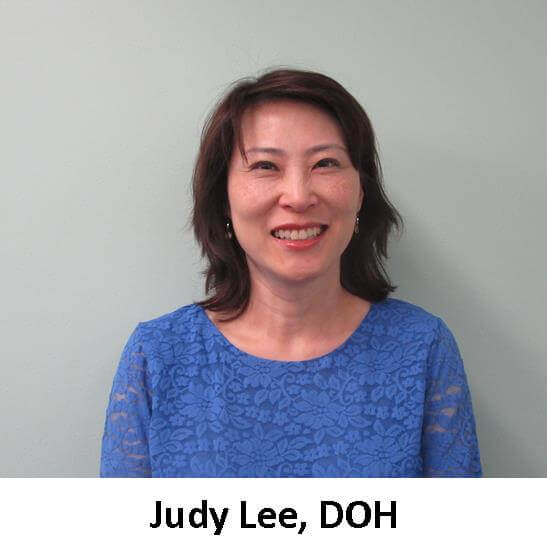 Judy lee, doh, smiling in front of a wall.