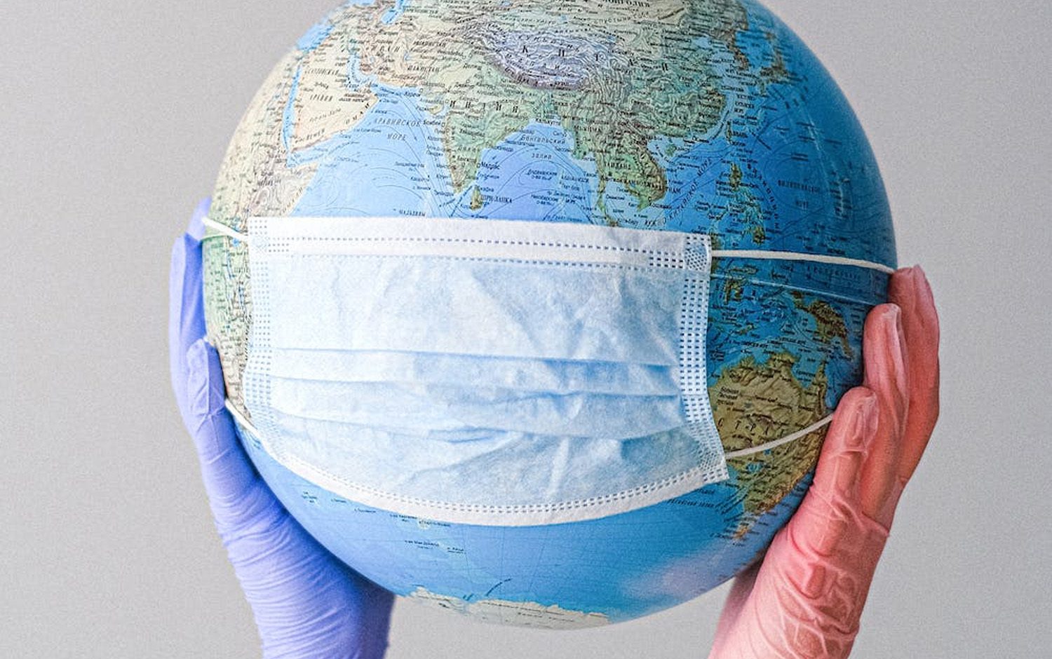 A hand holding a globe with a surgical mask on it.