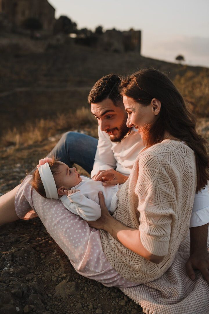 A family sits on a hill with a baby in their arms.
