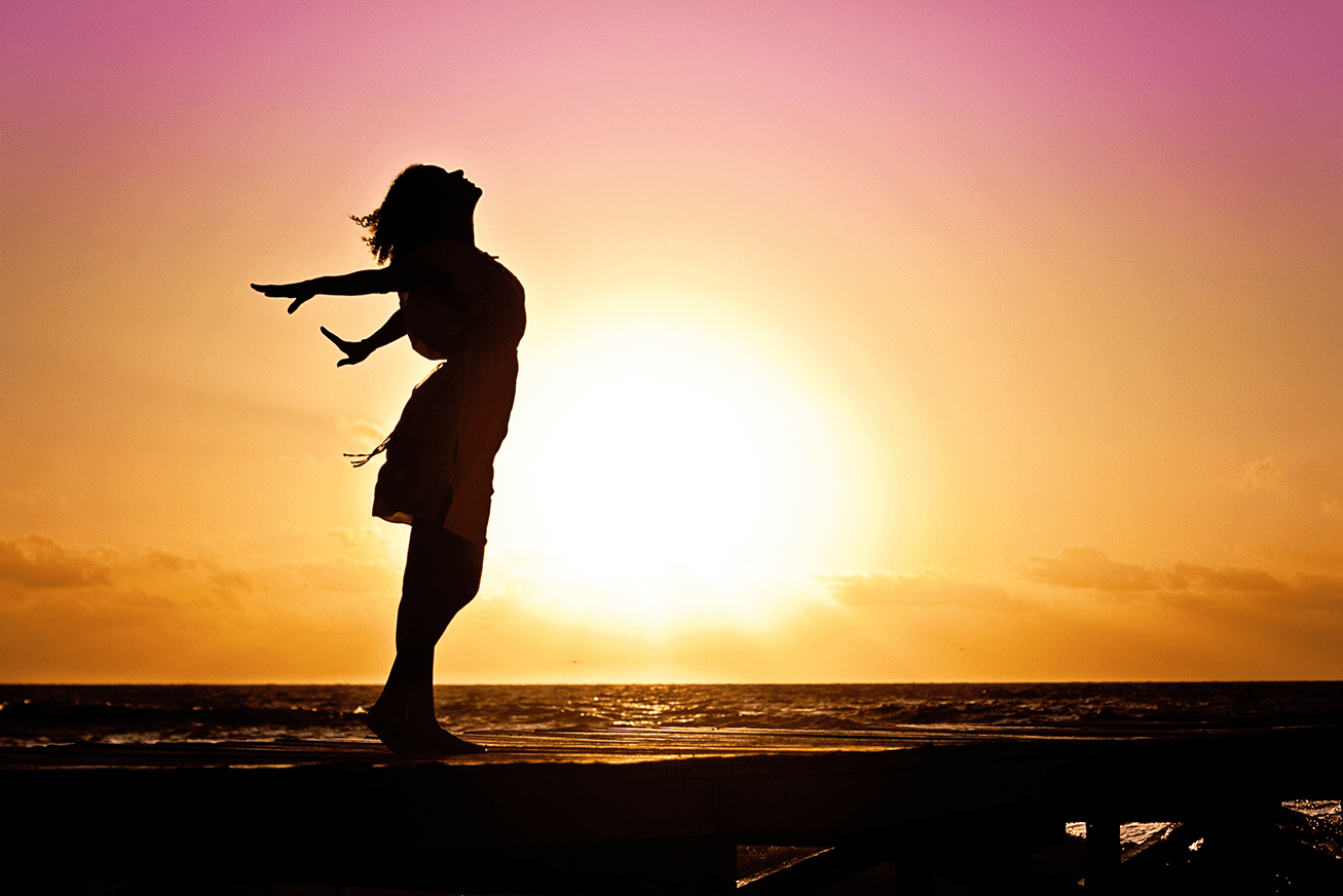 A silhouette of a woman standing on a dock at sunset.