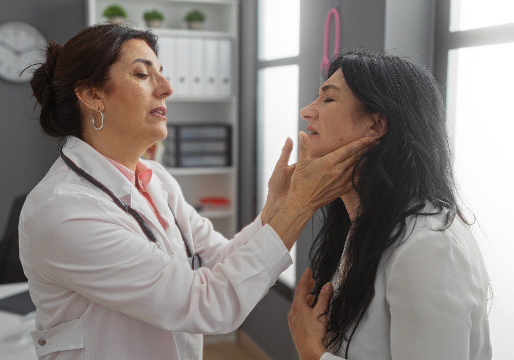 Mature female doctor examines woman's throat in a modern clinic interior.