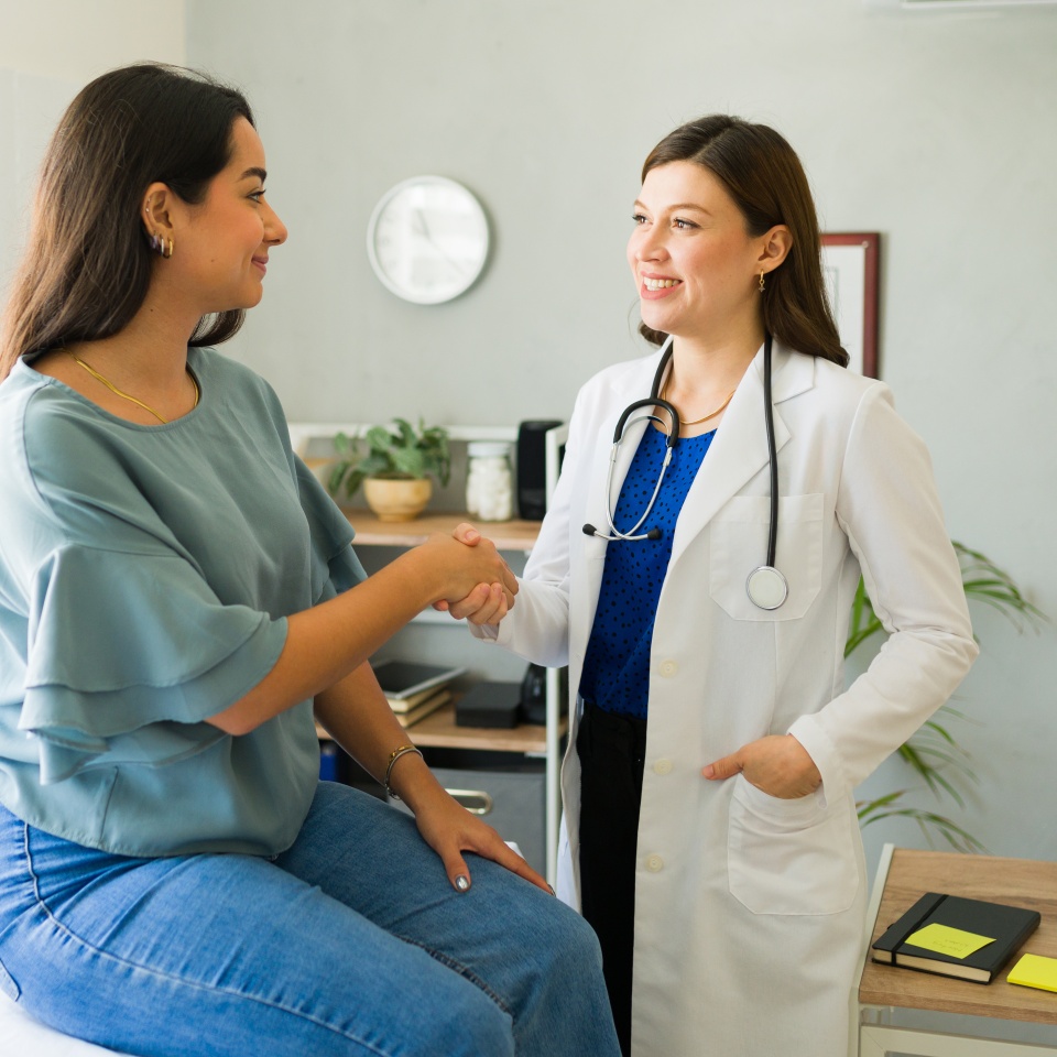 Female doctor happily shaking hands with her hispanic patient after a successful consultation in her office