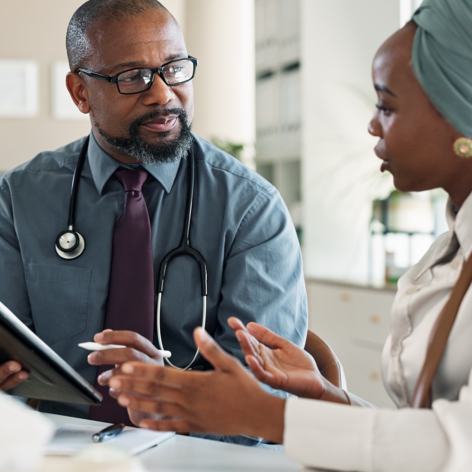 Tablet, consultation and black woman with doctor in hospital for medical diagnosis or wellness advice. Discussion, digital technology and female patient with healthcare worker for checkup in clinic