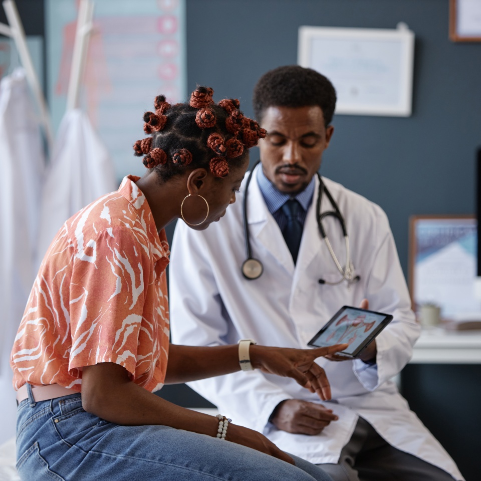 Side view of adult African American woman pointing at the screen during consultation with doctor in clinic and asking questions about treatment, copy space