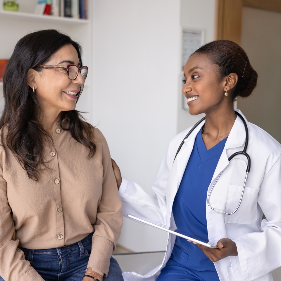 Happy supportive young African doc touching shoulder of senior woman on examination meeting in hospital office, congratulating on successful therapy, getting better, good checkup