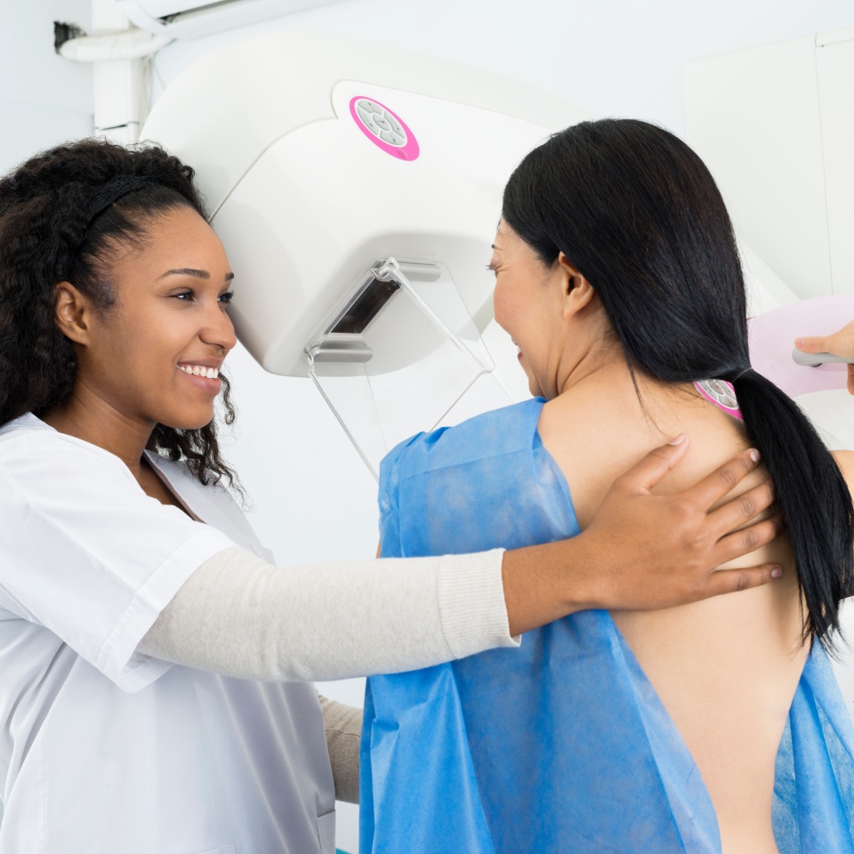 Happy female doctor assisting mature woman undergoing mammogram X-ray test in hospital