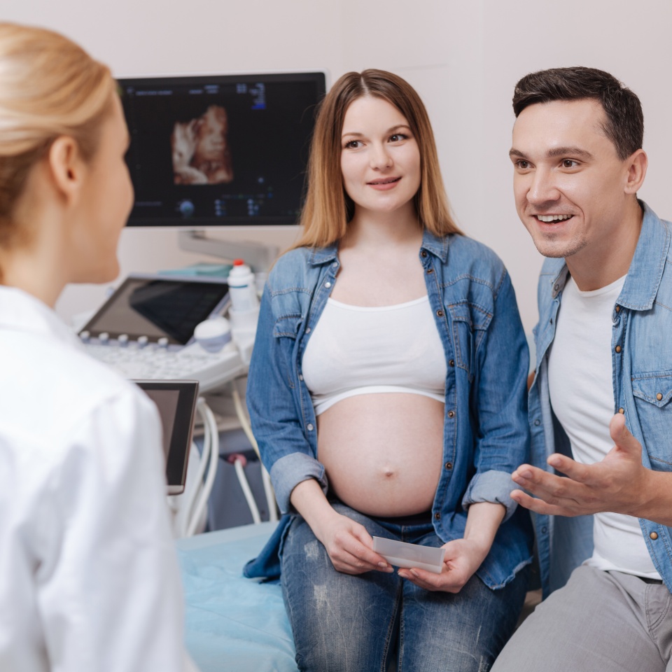 Expressing positivity together . Delighted involved professional medical specialist working in the clinic and having conversation with young couple while discussing future childbirth