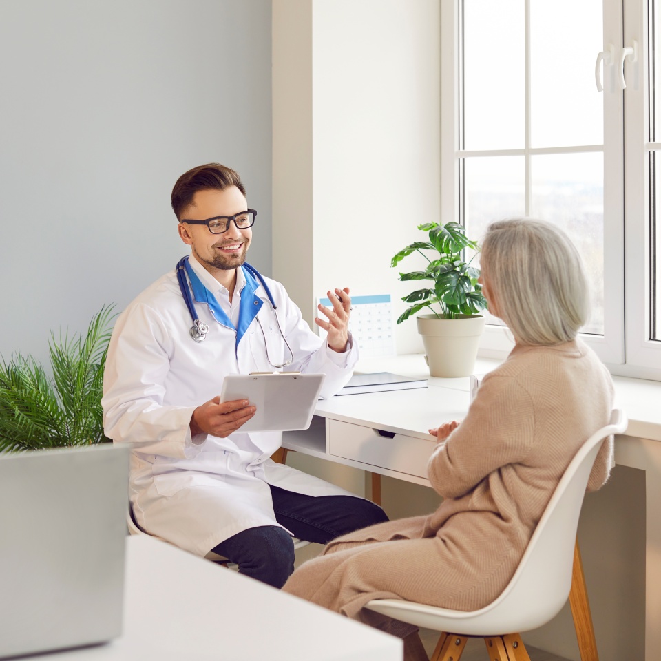Positive doctor or nurse is talking to an elderly patient during a hospital visit. The medical professional is providing healthcare and therapy, engaging in a conversation with the patient.