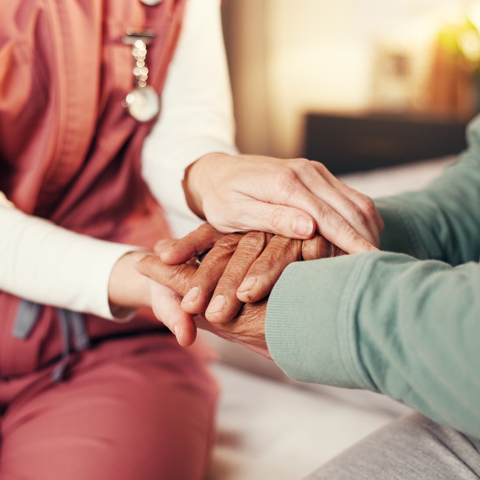 Caregiver, senior man and holding hands in home for medical service, empathy and compassion. Assisted living, night and nurse with comfort to elderly patient on bed for healthcare support and bonding.