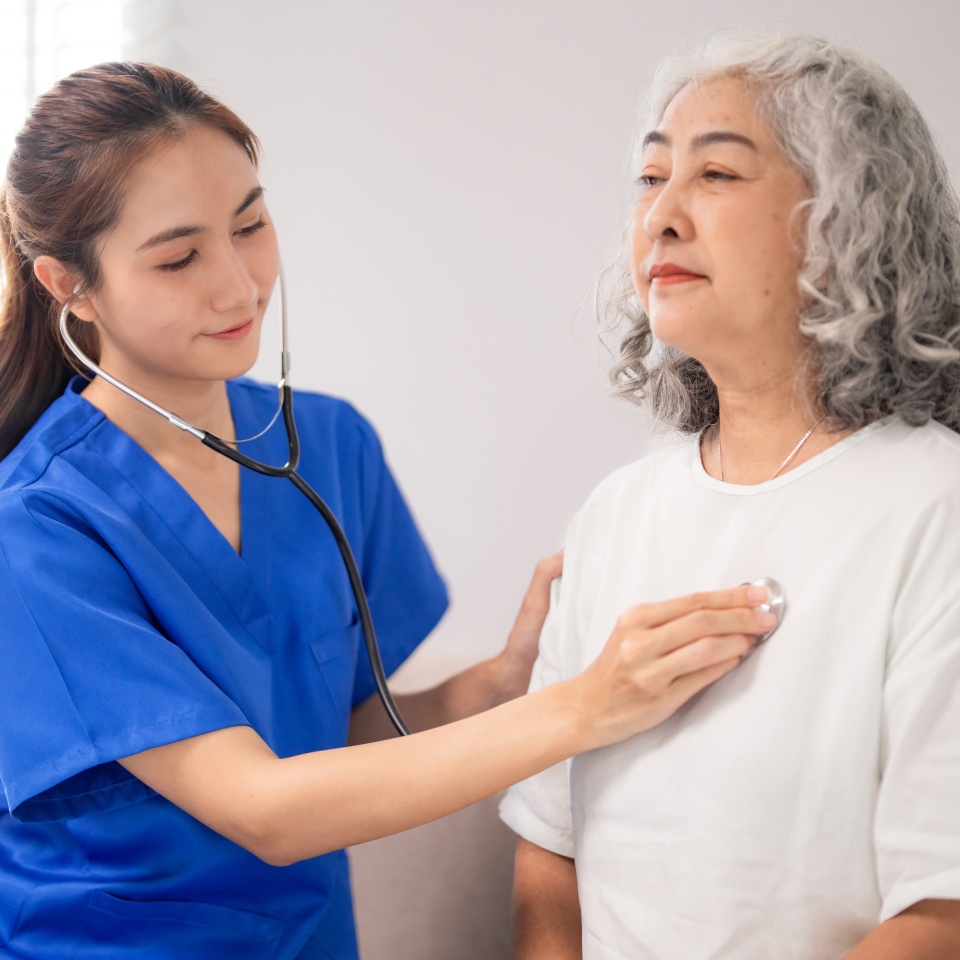 A compassionate Asian nurse attentively examines an older patient's heart with a stethoscope providing dedicated care and support