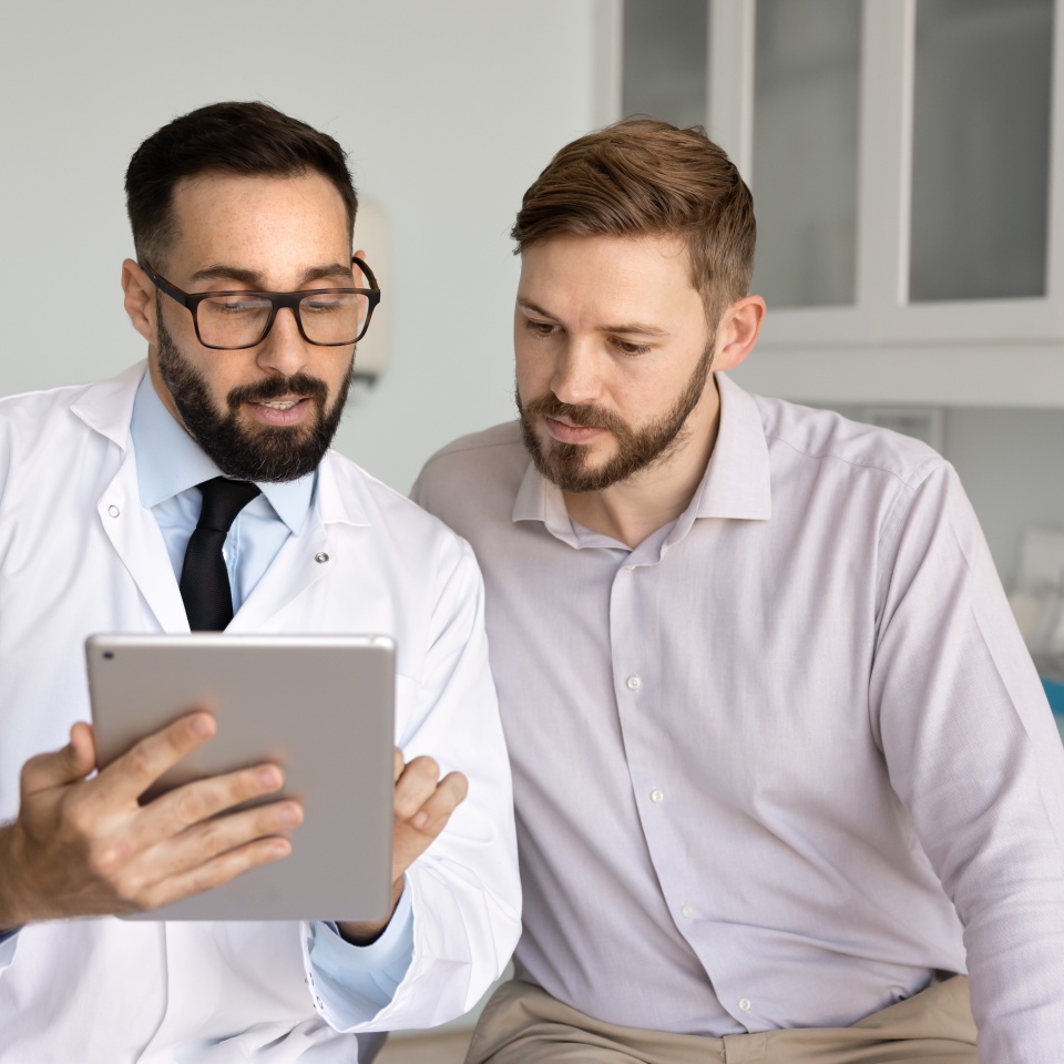 Digital tools on health consultation. Male medical professional communicate with patient in clinic office show prescribed medications list on digital device give recommendations using electronic chart