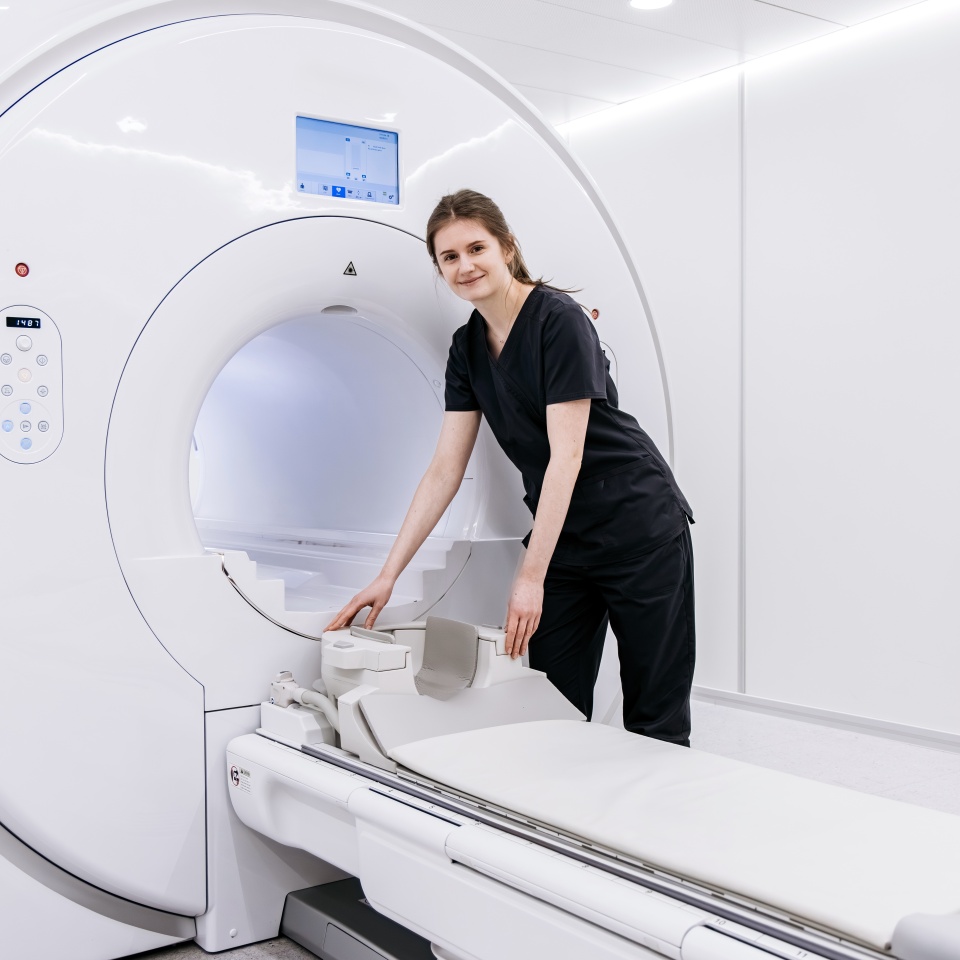 Female technician in black scrubs adjusts MRI machine in a modern medical facility, highlighting advanced imaging equipment and a sterile environment