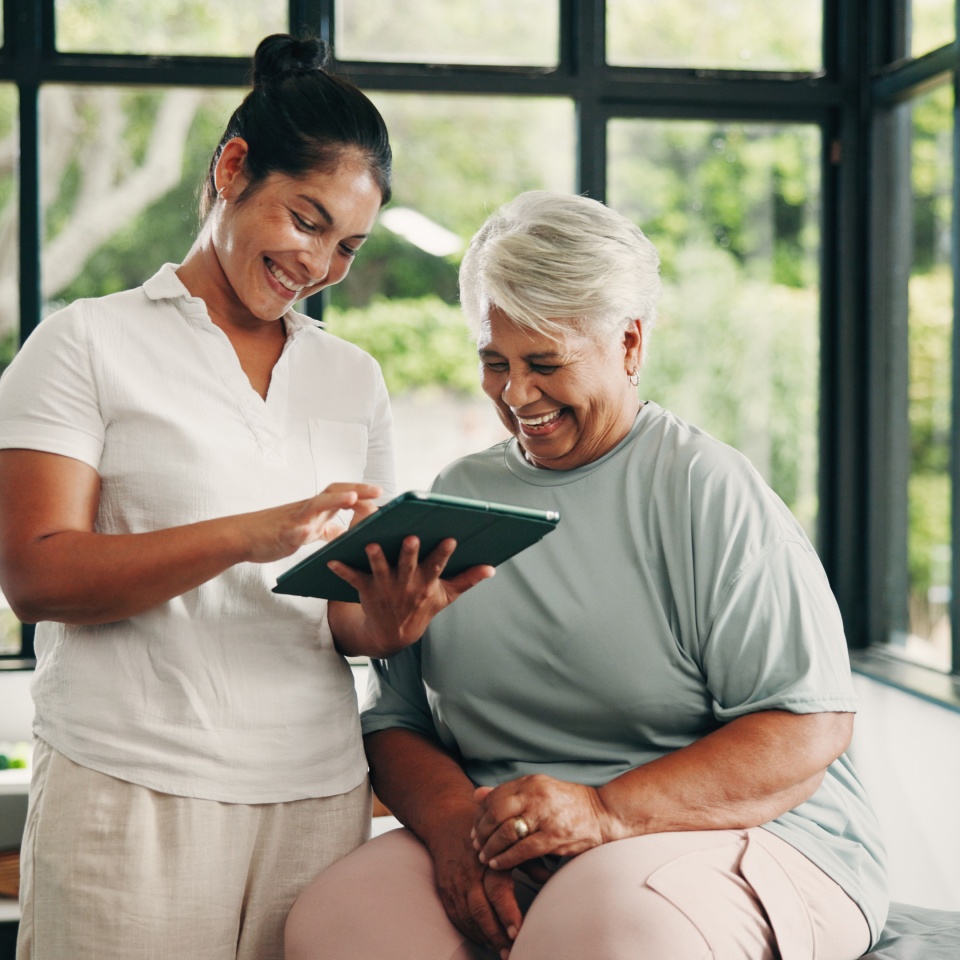 Tablet, physiotherapist and old woman in consultation, laugh and medical results in clinic. Tech, physical therapy or senior patient with chiropractor for healthcare recovery, rehabilitation or funny.