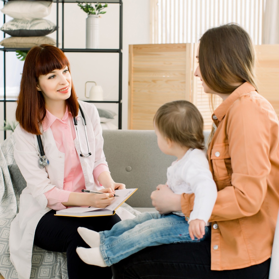 friendly young woman pediatrician doctor talks with mother of little baby girl after examination.