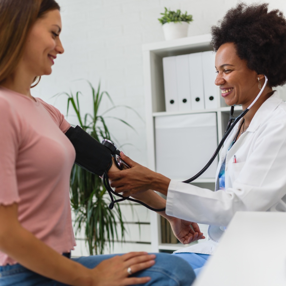 A healthcare professional measures a patient's blood pressure with a cuff in a medical office.