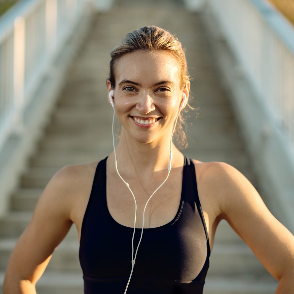 Portrait of happy athletic woman listening music on earphones and looking at camera.