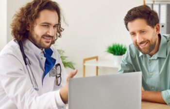 Doctor explains results of tests or treatment protocol of disease to male patient on laptop. Male doctor showing medical diagnosis report and giving medical consultation to man. Healthcare concept.