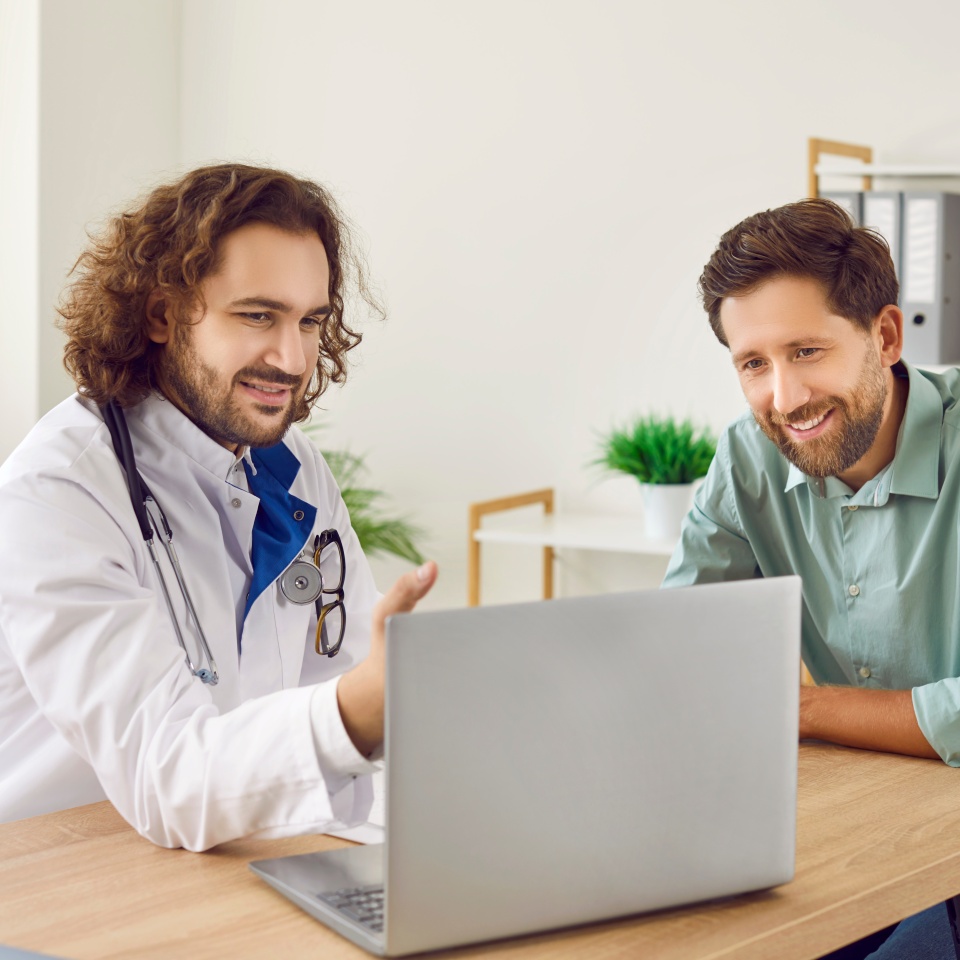 Doctor explains results of tests or treatment protocol of disease to male patient on laptop. Male doctor showing medical diagnosis report and giving medical consultation to man. Healthcare concept.