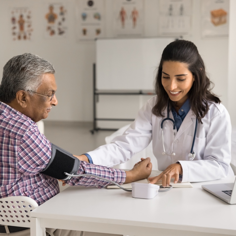 Positive young cardiologist doctor woman examining elderly geriatric patient, checking blood pressure rate, using electronic gadget , cardiology instrument for measuring, diagnosing, checkup