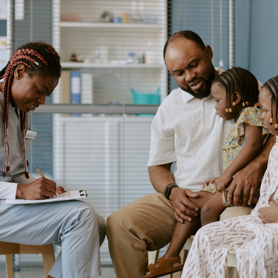 Medical professional attentively engaging with father and two children in clinic setting having a detailed discussion about health and wellbeing