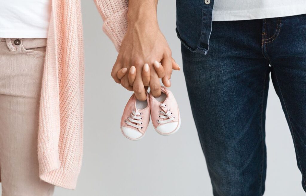 A couple holding hands and carrying baby's shoes between them