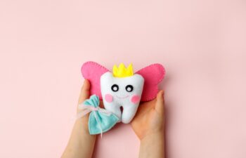 Little child holding felt tooth fairy toy in his hands on pink background. Easy and funny kids crafts, DIY, Happy Tooth Fairy greeting card, flyer, copy space, concept of tooth changes
