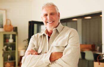 Arms crossed, smile and portrait of old man in home for retirement, peace and confidence. Happiness, calm and weekend break with senior person in living room of apartment for positive attitude.