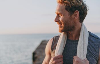 Close up happy young strong sporty athletic toned fit sportsman man in sports clothes towel warm up train look aside at sunrise sun dawn over sea beach outdoor on pier seaside in summer day morning.