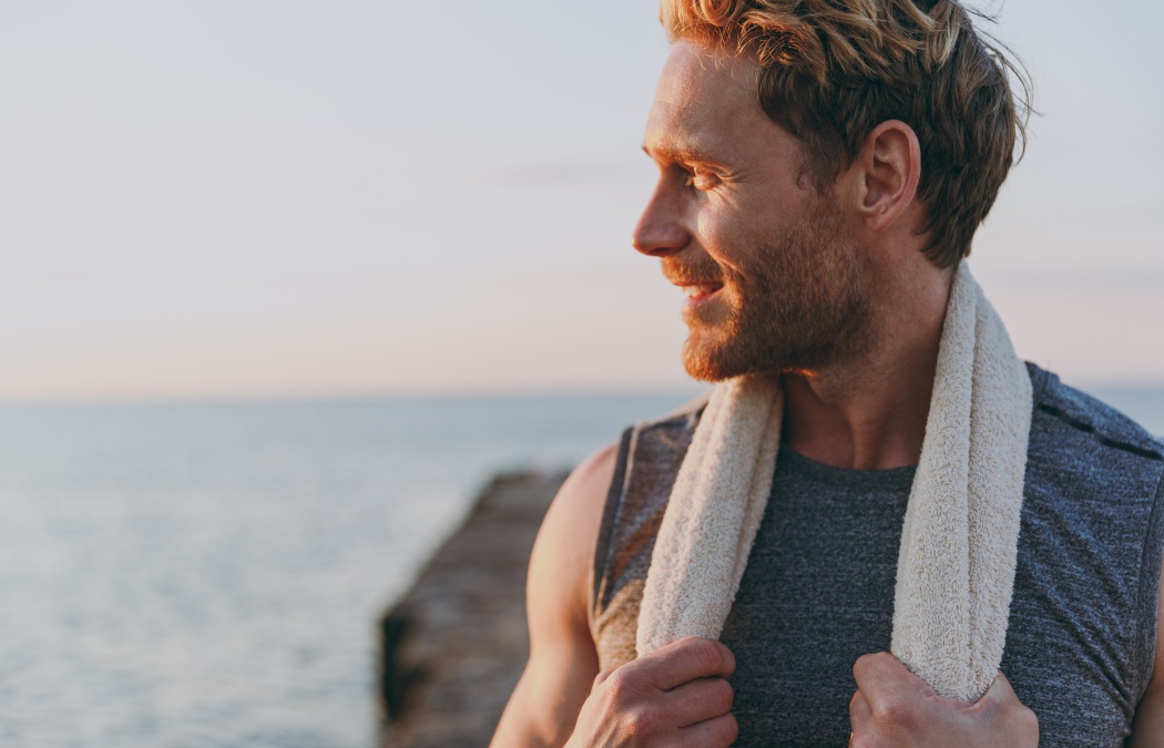 Close up happy young strong sporty athletic toned fit sportsman man in sports clothes towel warm up train look aside at sunrise sun dawn over sea beach outdoor on pier seaside in summer day morning.